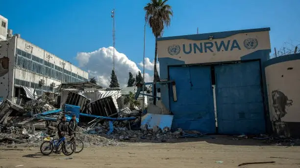 Warga Palestina berjalan melintasi Kantor Badan PBB untuk Pengungsi Palestina (UNRWA) di Kota Gaza yang rusak.