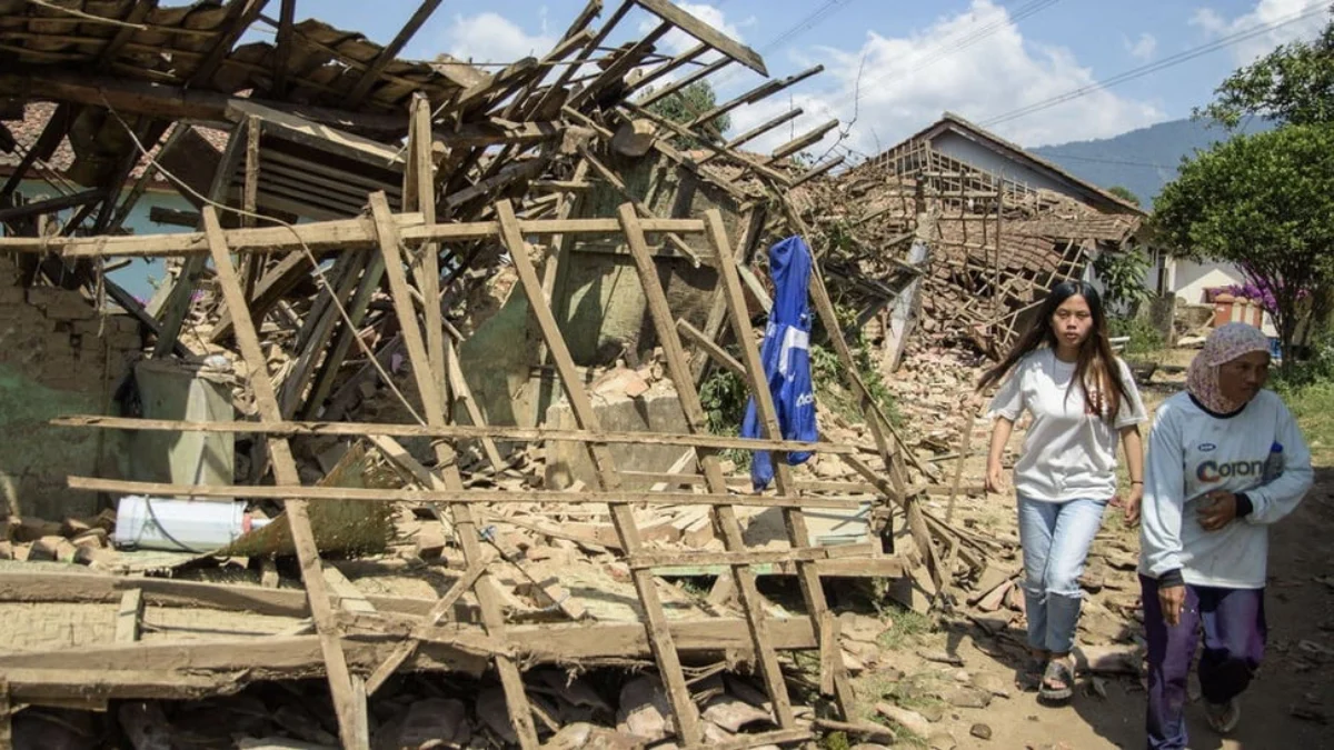 Warga melintas di dekat rumah yang rusak pascagempa bumi di Desa Cibeureum, Kertasari, Kabupaten Bandung, Jawa