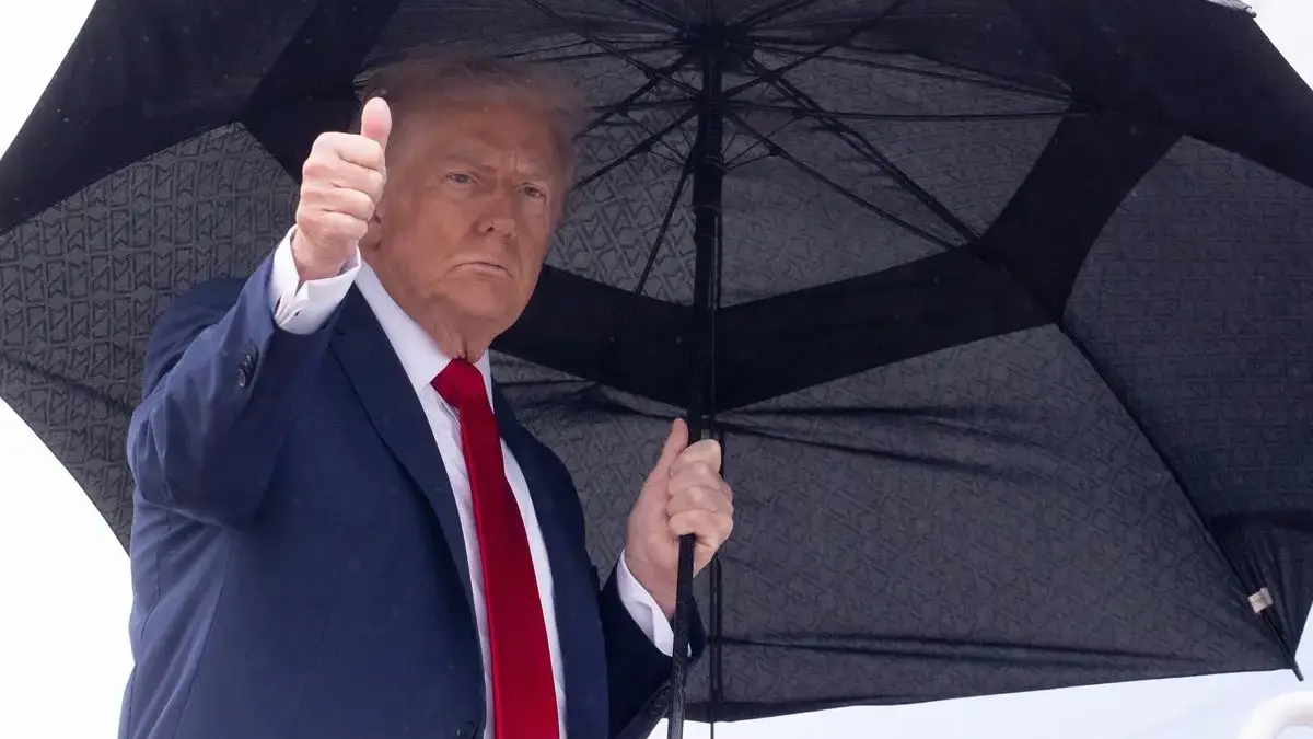 Presiden Amerika Serikat Donald Trump mengacungkan jempol sambil membawa payung saat akan menaiki pesawat kepr